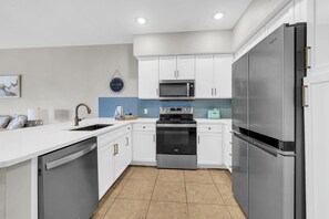 A modern kitchen with white cabinetry, stainless steel appliances, and a blue backsplash. - Village at Blue Mtn Beach 625 - Close to beach located in 30A (Santa Rosa Beach)