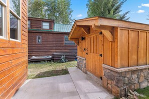 A wooden cabin with a stone foundation, a concrete pathway, and a green roof.