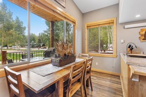 A wooden dining table with chairs, a wicker basket, and a view of a park with trees and a pathway.