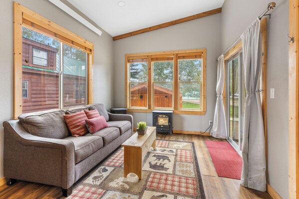 A cozy living room with a sofa, a small table, a fireplace, and large windows.