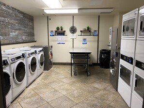 A laundry facility with multiple washing machines, a table with a trash bin, and a clock on the wall. - Family Cabin in Breckenridge Tiger Run Resort 5 min to Gondola (Breckenridge)