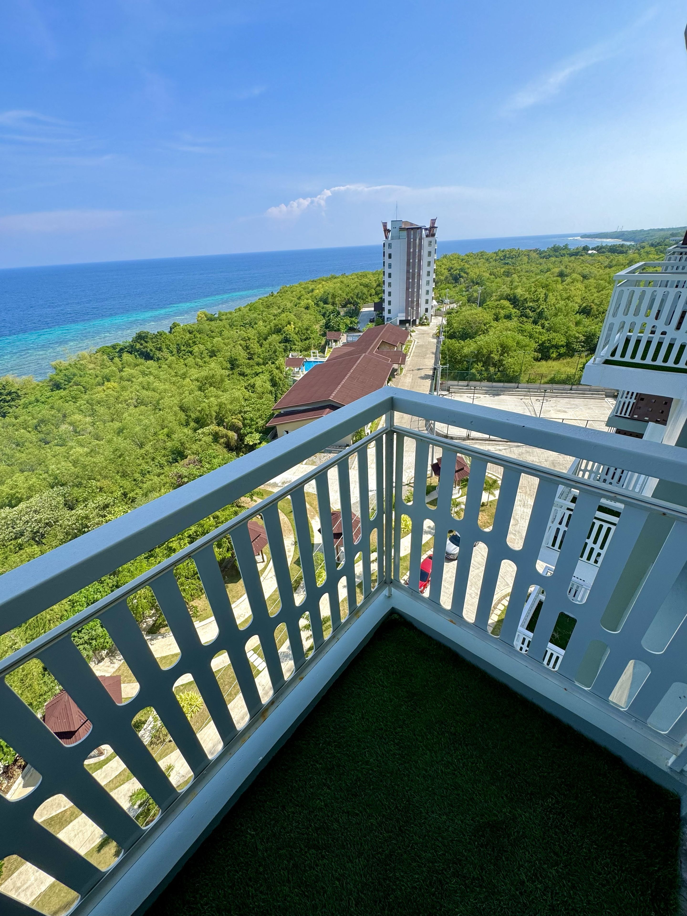 A balcony with a view of a coastal area, including a building and a clear sky.