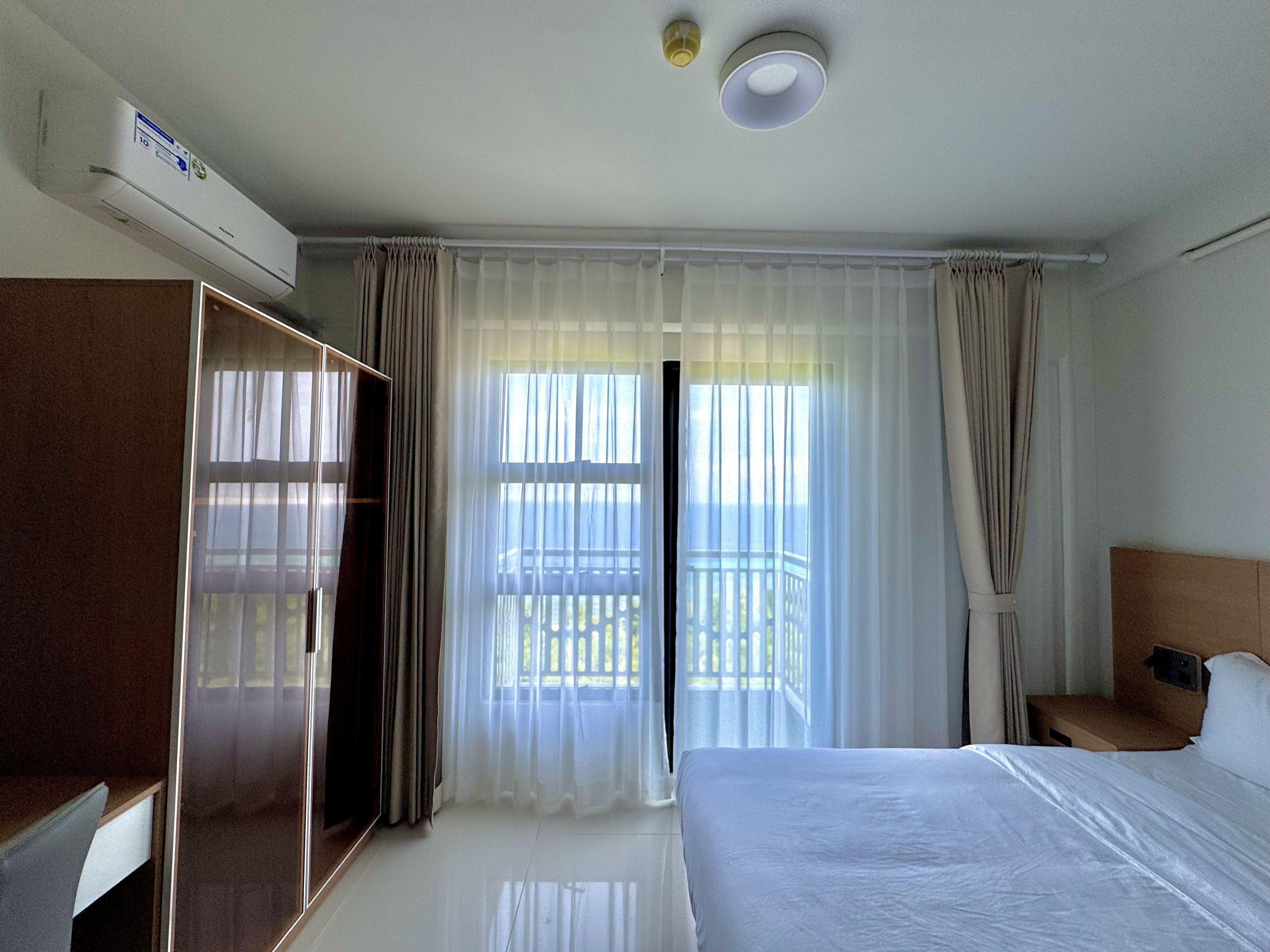 Habitación de hotel con cama, armario, escritorio y balcón con cortinas.