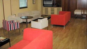 Quarto de hotel com sofá, poltronas, uma mesa pequena, televisão e cozinha compacta.