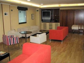Habitación de hotel con sofá, sillones, una mesita, televisión y kitchenette.