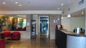 Um saguão de hotel com balcão de recepção, área de estar e um elevador de vidro.