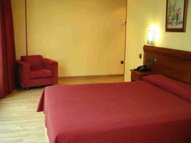 Una habitación de hotel con cama, una silla, una mesita de noche y una lámpara fijada a la pared.
