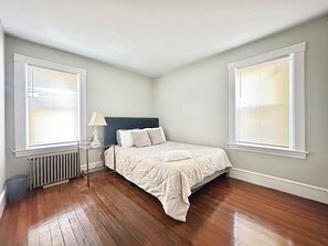 A bedroom with a bed, a nightstand, a lamp, and a radiator. - Spacious 3B2B home near JWU & Roger Williams Park (Providence)