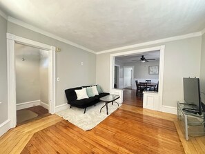 A living room with a black sofa, a white rug, and a dining area with a table and chairs. - Spacious 3B2B home near JWU & Roger Williams Park (Providence)