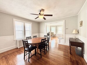 A dining room with a wooden table and chairs, a ceiling fan, and a view into another room. - Spacious 3B2B home near JWU & Roger Williams Park (Providence)