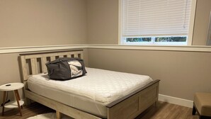 Un dormitorio con una cama, una mesita redonda pequeña, un tapete blanco y esponjoso y una ventana con persianas.