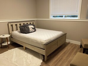 Une chambre à coucher avec un lit, une petite table ronde, un tapis blanc et moelleux, et une fenêtre avec des stores.