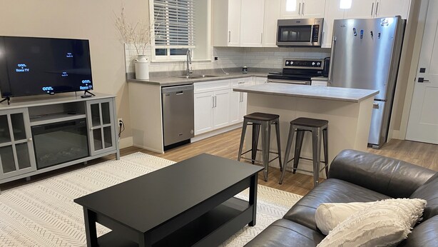 Una cocina moderna con microondas, refrigerador y lavavajillas. Hay un comedor con una mesa negra y un sofá de cuero.