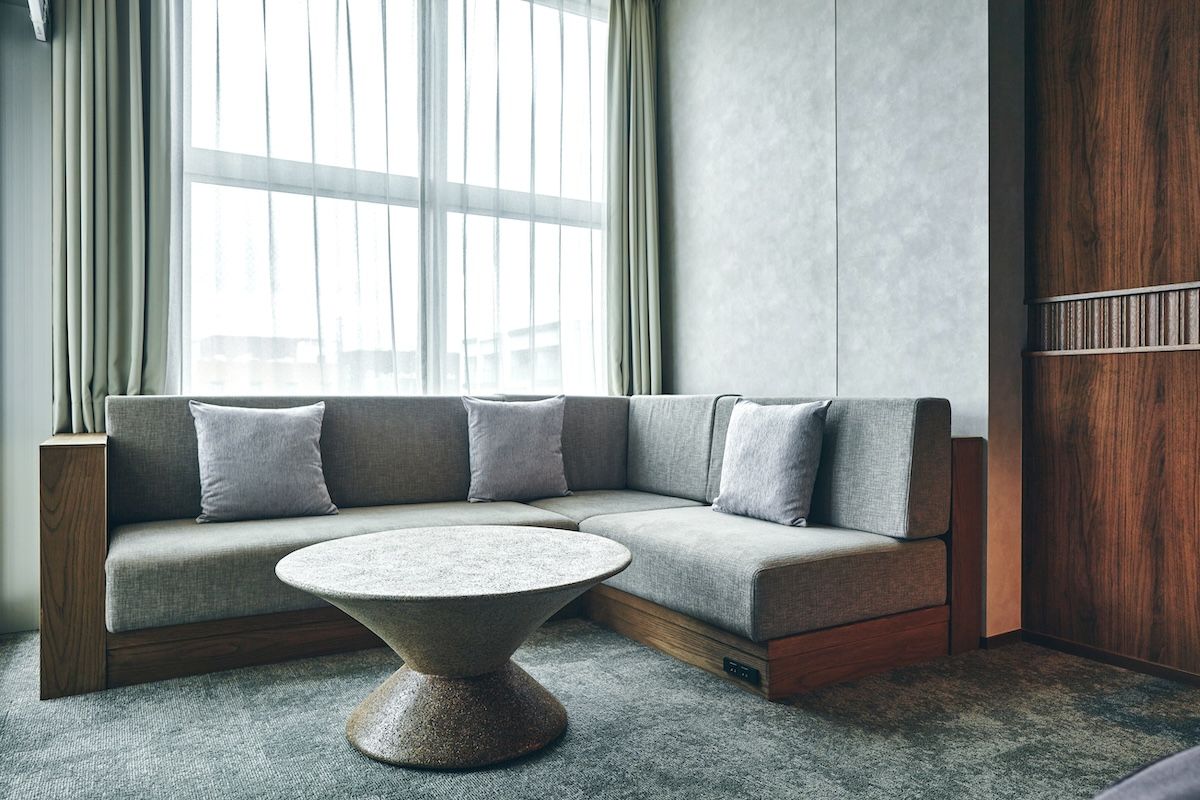 Uma sala de estar moderna com sofá seccional, mesa de centro redonda e uma janela grande com cortinas.