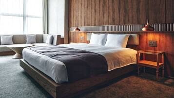 Quarto moderno com cabeceira de madeira, cama grande, mesa de cabeceira e um espaço de estar com um banco.