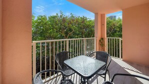 A balcony with a glass table and four chairs, surrounded by a white railing, overlooking a tree-lined area. - Charming 3 Bedroom Apartment in Aventura - Cozy and Beautifull, Ideal for Family (Aventura)