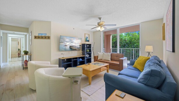 A living room with a sofa, coffee table, and TV. There's a balcony with a railing and a view of greenery. - Charming 3 Bedroom Apartment in Aventura - Cozy and Beautifull, Ideal for Family (Aventura)