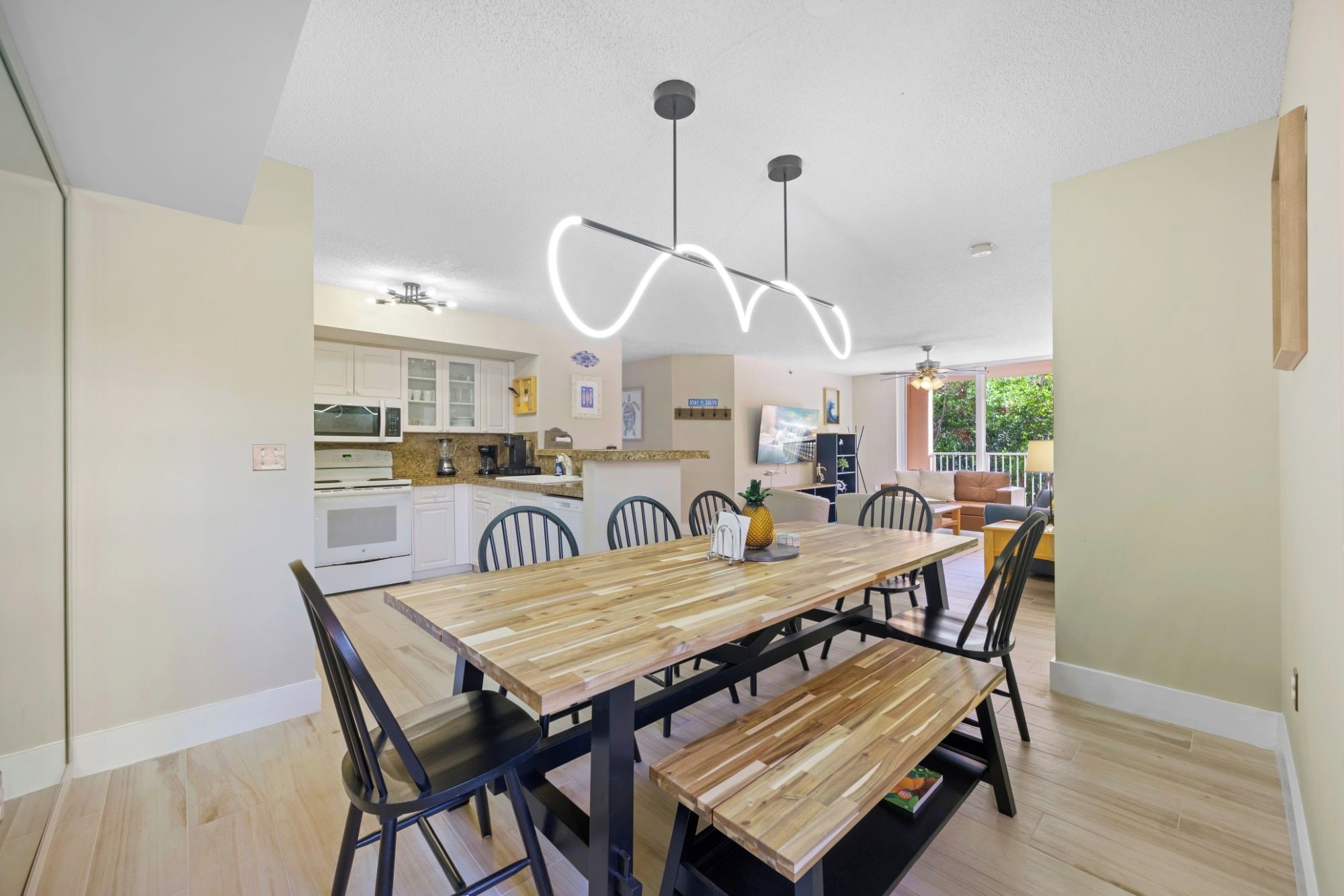A modern kitchen with white cabinets, a dining area with a wooden table and chairs, and a ceiling light fixture.