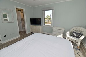 A bedroom with a bed, a television on a dresser, a window, and a wicker chair with a 'RELAX' pillow. - Game Time Up (Upstairs Only) - Walk to the Beach (Garden City Beach)