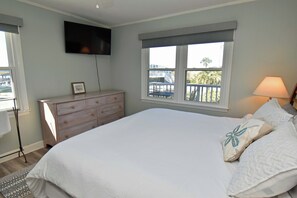 A bedroom with a large bed, a dresser, a TV mounted on the wall, and a window with a view of a balcony. - Game Time Up (Upstairs Only) - Walk to the Beach (Garden City Beach)