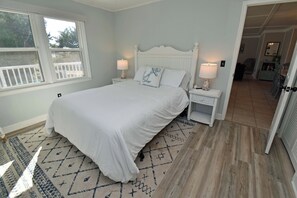 A bedroom with a large bed, two bedside tables with lamps, a patterned rug, and a view of the outdoors through a window. - Game Time Up (Upstairs Only) - Walk to the Beach (Garden City Beach)