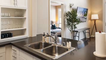 A modern kitchen with stainless steel sinks, a countertop with glassware, and a dining area with a table and chairs.