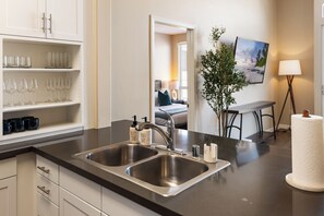 A modern kitchen with stainless steel sinks, a countertop with glassware, and a dining area with a table and chairs.