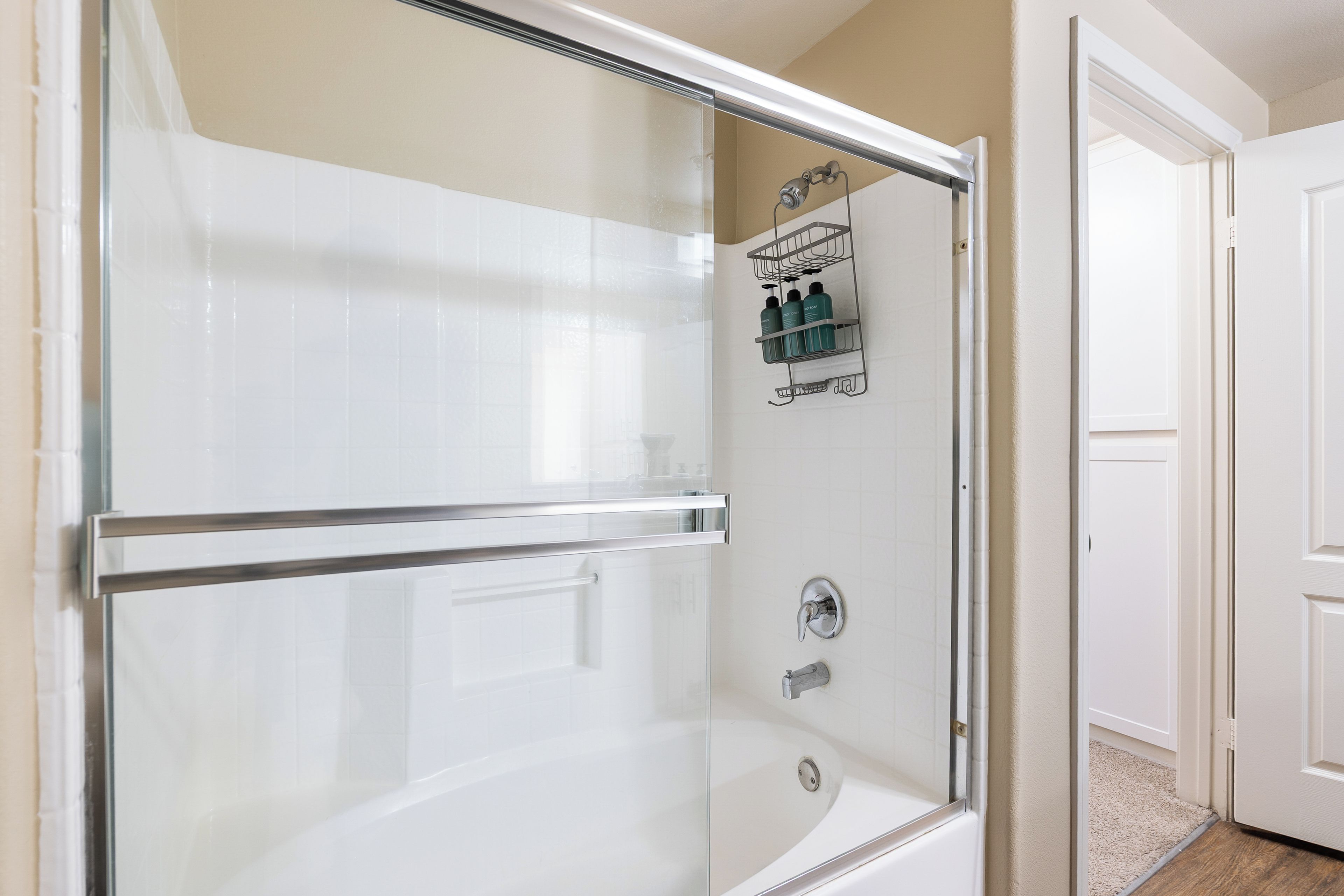 Ein Badezimmer mit einer gläsernen Duschkabine, einer weißen Badewanne und einem Duschkörbchen mit Pflegeprodukten.