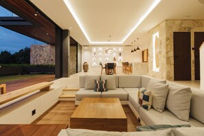 A modern living room with a large sectional sofa, a wooden coffee table, and a dining area with a table and chairs. - Villa Santi Bayu by Alfred in Bali (Pecatu)