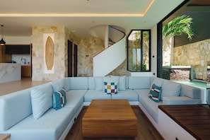 A modern living room with a light-colored sectional sofa, a wooden coffee table, and a stone accent wall. - Villa Santi Bayu by Alfred in Bali (Pecatu)