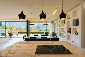 Ein modernes Interieur mit einem großen Esstisch aus Marmor, schwarzen Pendelleuchten und Blick ins Freie.