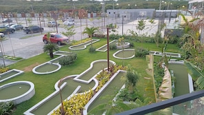 Un campo de mini golf con varios hoyos, rodeado de zonas ajardinadas y un estacionamiento.