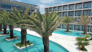 Ein modernes Hotel mit Schwimmbad, umgeben von Palmen, und ein mehrstöckiges Gebäude mit Balkonen.