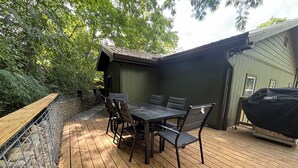 Um pátio externo com deck de madeira, uma mesa com cadeiras e uma churrasqueira.