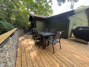 Eine Außenpatio mit Holzterrasse, einem Tisch mit Stühlen und einem Grill.
