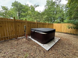 Ein Whirlpool in einem Garten mit Holzzaun und Bäumen im Hintergrund.