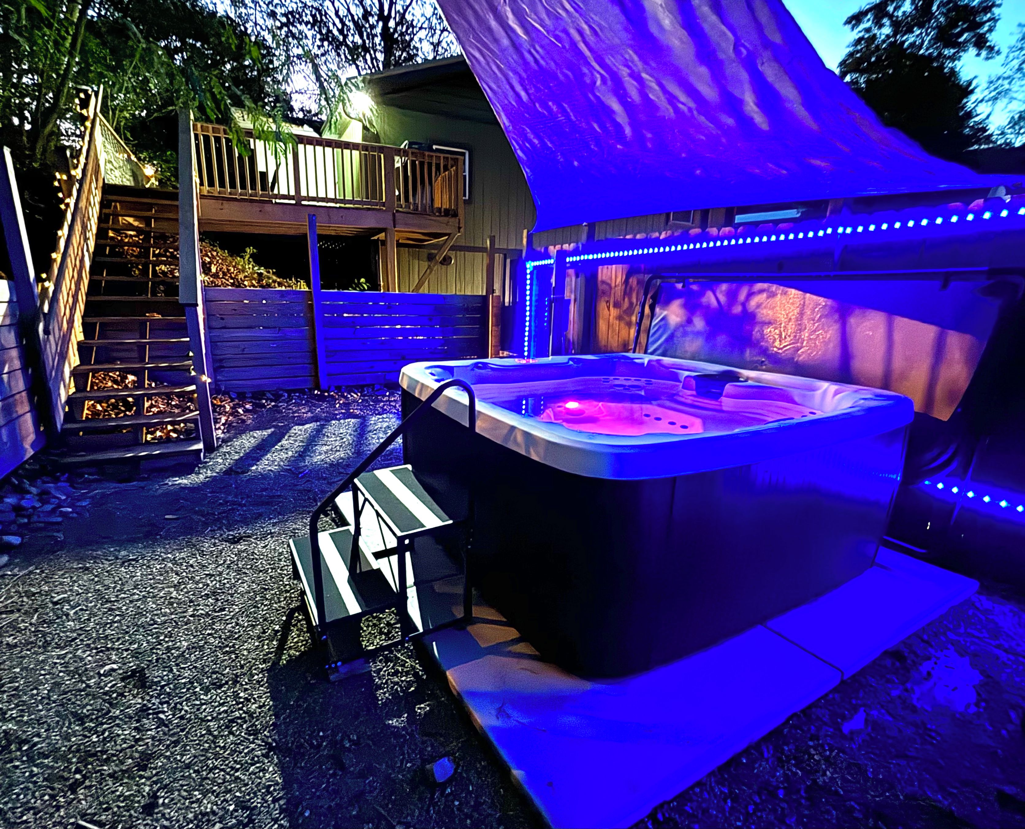 A hot tub with a wooden deck and a covered area with blue LED lights.