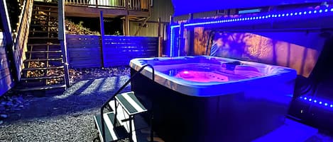 A hot tub with a wooden deck and a covered area with blue LED lights.