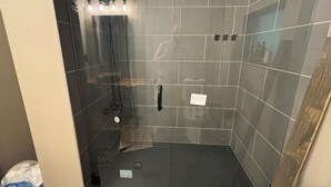 Chuveiro com porta de vidro, barra de apoio e parede revestida em azulejo.