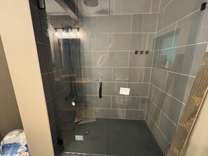 Eine Dusche mit Glastür, Handlauf und gefliesten Wänden.
