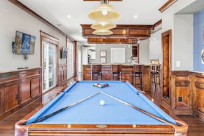 A pool table with a blue felt surface, wooden surroundings, and a pool cue. - The Regency | Oceanfront | Private Pool (Virginia Beach)