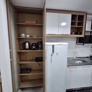 Une cuisine avec des étagères en bois, un réfrigérateur blanc, une machine à café et un évier.