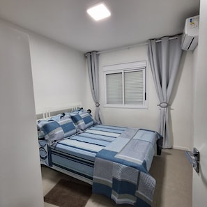 Une chambre à coucher avec un lit, des rideaux, une fenêtre et un appareil de climatisation.