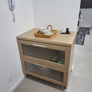 Une table de chevet en bois sur laquelle repose un panier tressé contenant une tasse, un bol et une cuillère.