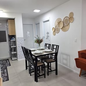 A dining area with a table set for four, surrounded by chairs, a vase with flowers, and a wall with woven decorations.