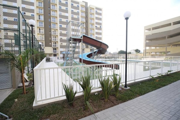 Un quartier résidentiel avec une piscine, une clôture blanche et un immeuble à plusieurs étages en arrière-plan.
