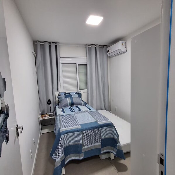 A bedroom with a bed, curtains, an air conditioning unit, and a nightstand with a lamp. - Fantastic accommodation. Central Apartment (Pelotas)