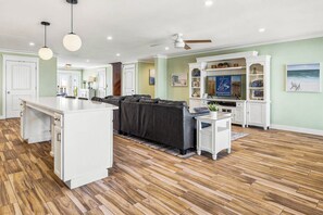 A spacious living area with a central island, a dark sofa, and a white entertainment unit. - The Regency Royale | Oceanfront | Private Pool (Virginia Beach)