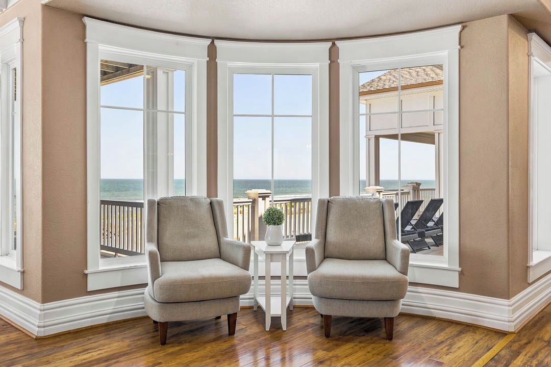 A corner room with two armchairs, a small table, and a view of the ocean.