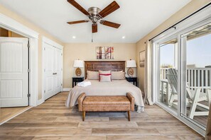 A bedroom with a large bed, a ceiling fan, a bench, and a balcony with a railing. - The Regency Royale | Oceanfront | Private Pool (Virginia Beach)